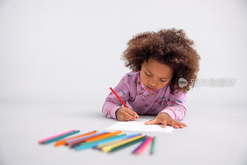 小女孩用彩色铅笔在地板上画画