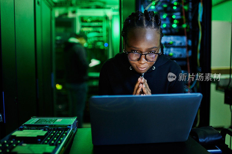 一名年轻的女电脑程序员站在黑暗的服务器室里使用笔记本电脑