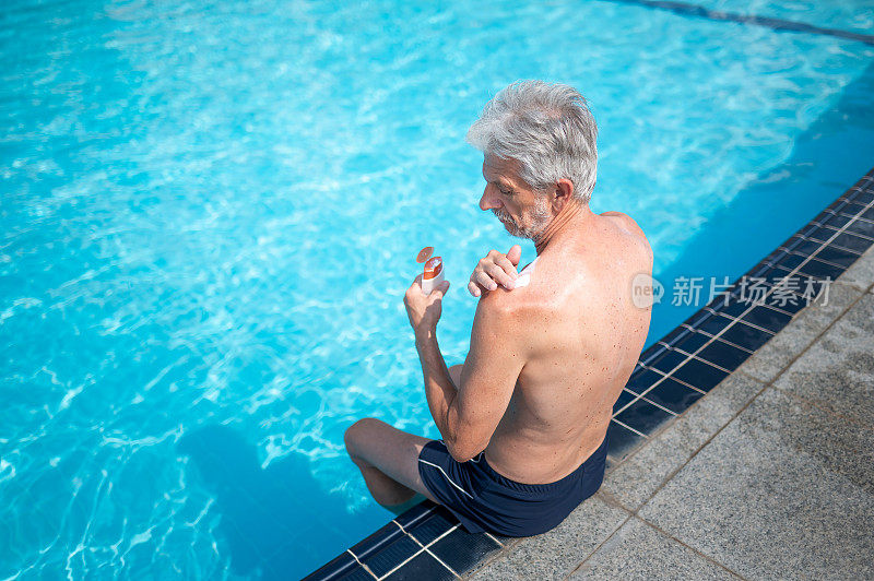 在游泳池边休息和晒黑的时候，资深男士正在涂抹防晒霜保护皮肤