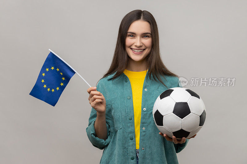 女子手持黑白相间的足球和欧盟国旗，观看足球比赛，支持自己喜欢的球队。