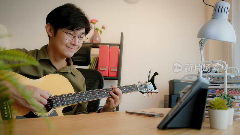 微笑的自由音乐家吉他手与钢琴家通过视频电话在家中演奏原声吉他。两名男子正在智能手机上通过远程办公技术进行音乐直播。