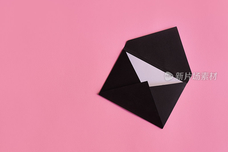 黑色信封与纸卡片在柔和的粉红色背景。邀请，贺卡，信件或愿望清单的概念