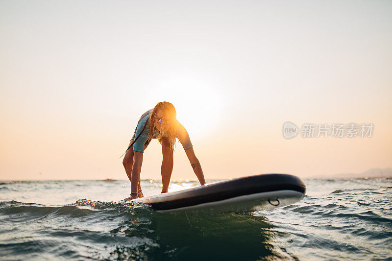 在冲浪时，一名女性冲浪者小心地站起来，试图在SUP板上保持平衡