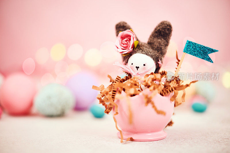 可爱的手工制作的复活节兔子在一个蛋杯里面，周围是复活节彩蛋和粉红色的背景