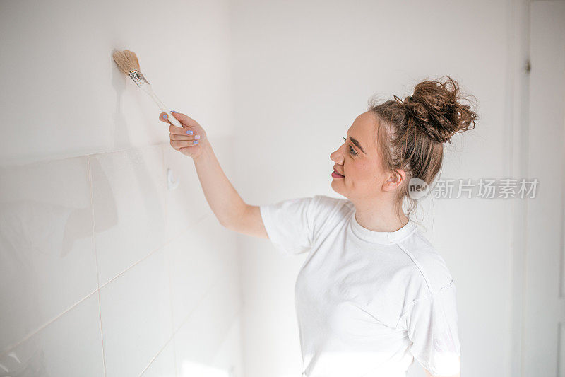 微笑的女人用刷子刷白色的墙