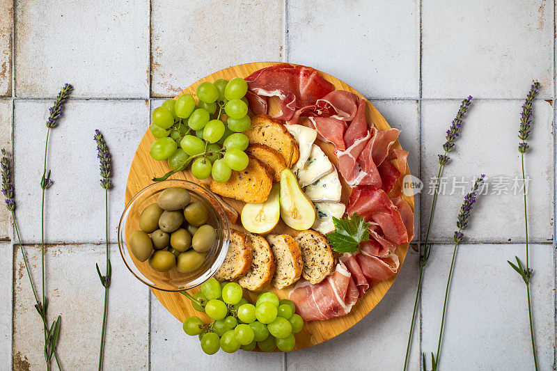 意大利熏火腿，意大利腊肠，烤面包，奶酪，橄榄，白葡萄和梨。盛在木制的圆板上。