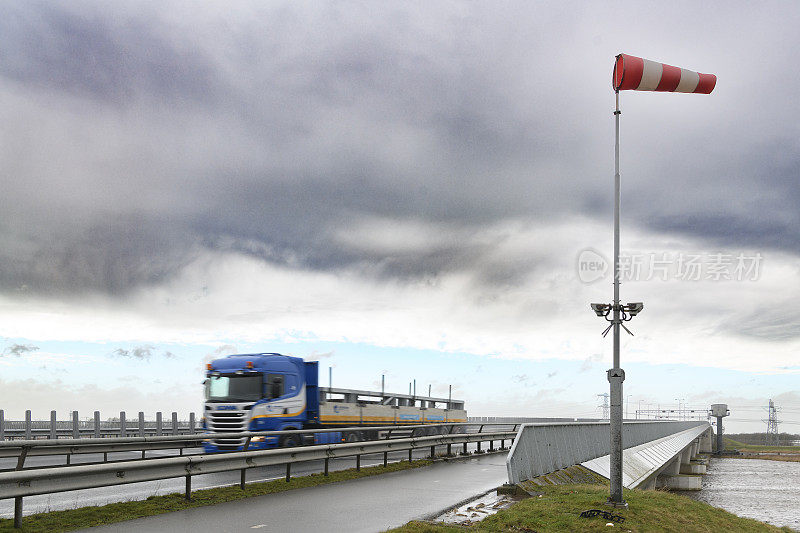 在暴风雨中，卡车在桥上行驶，桥上挂着风向标警告标志