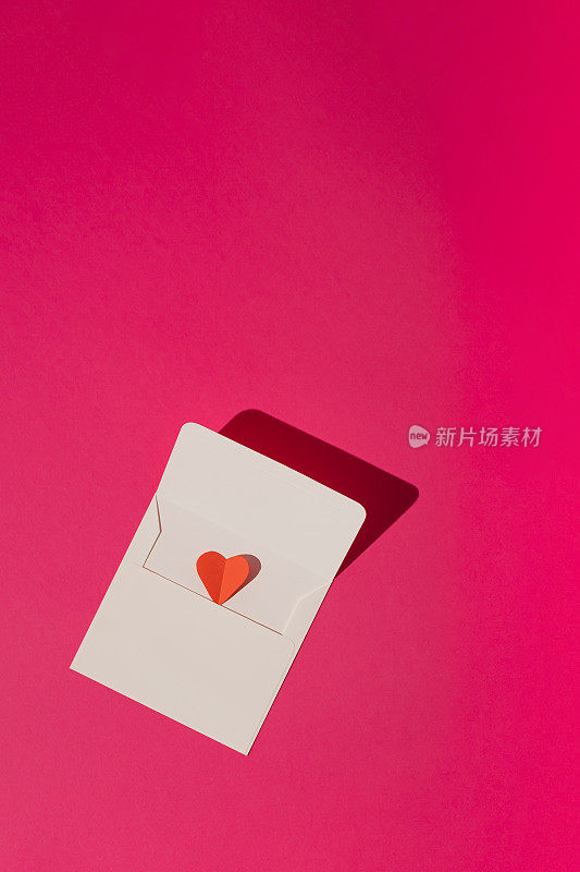 白色信封，红心在洋红色的粉红色背景。最小限度的爱或情人的概念。
