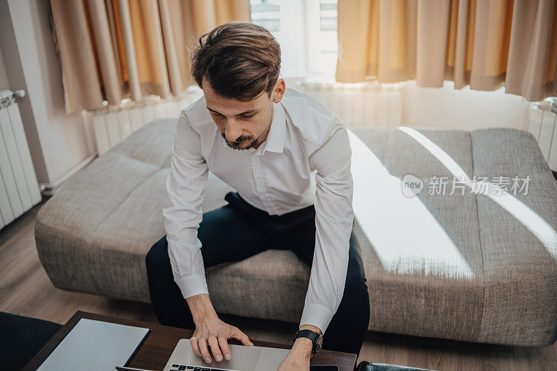 一名年轻的波兰男子穿着白衬衫，在酒店房间里用笔记本电脑上网