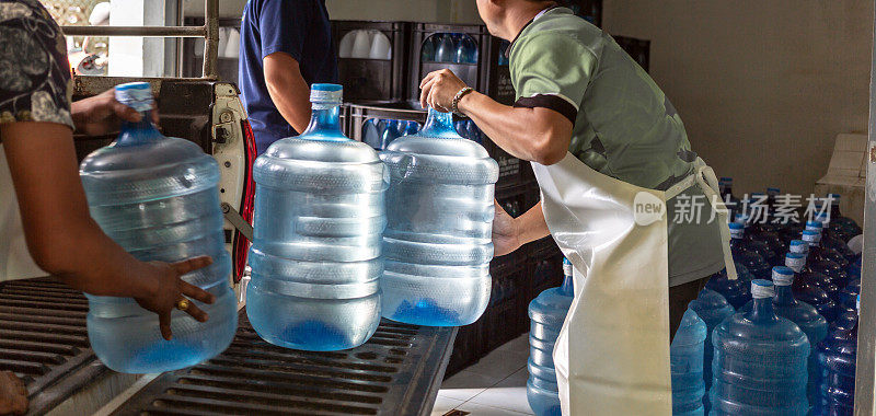 工人们把几加仑的蓝色饮用水和装在板条箱里的瓶子搬到一辆运输卡车的后面。