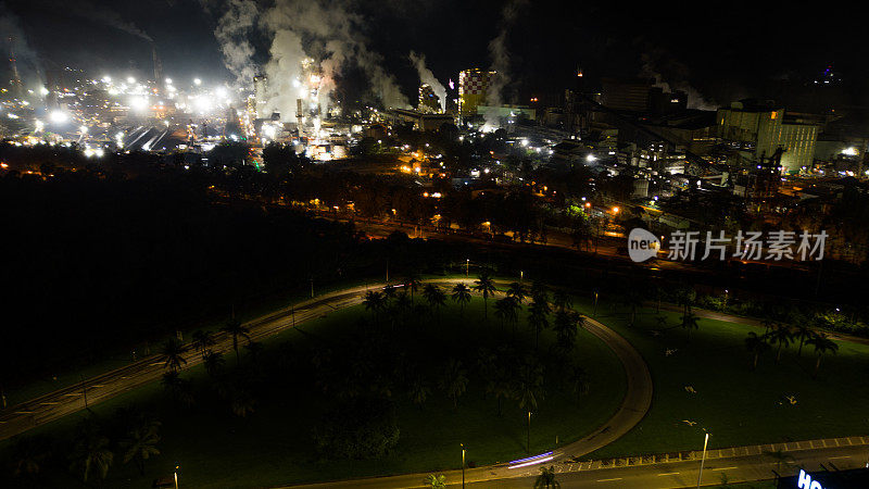 夜间城市鸟瞰图，背景是钢铁发电厂排放的烟雾