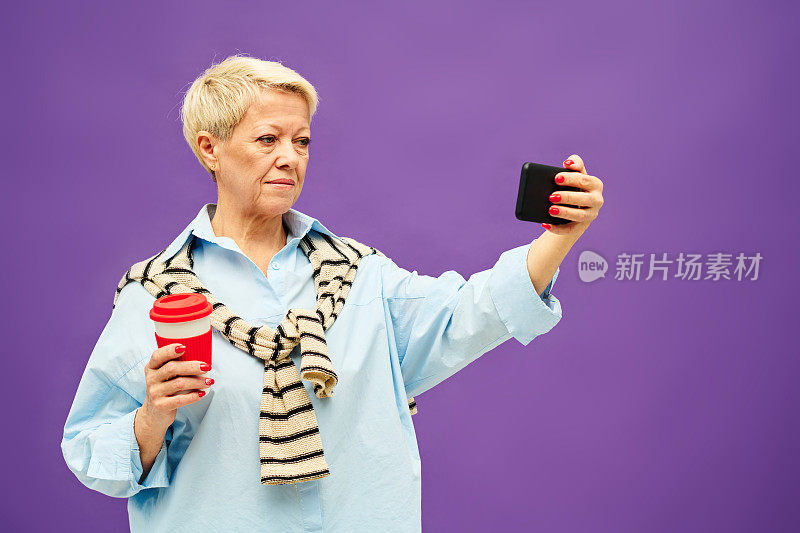 成熟的金发女人在便装喝咖啡和看在线视频