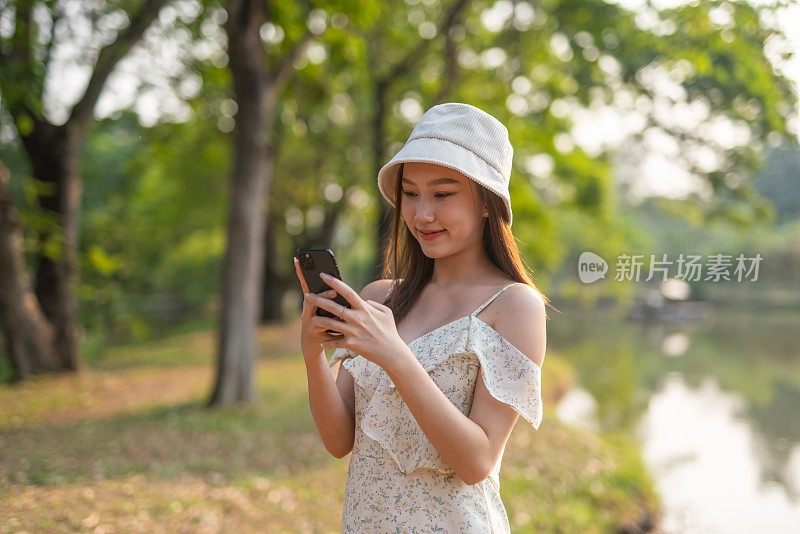 年轻的亚洲女子在公园里使用手机应用程序。美丽的女人在郁郁葱葱的绿色森林里查看手机上的应用程序