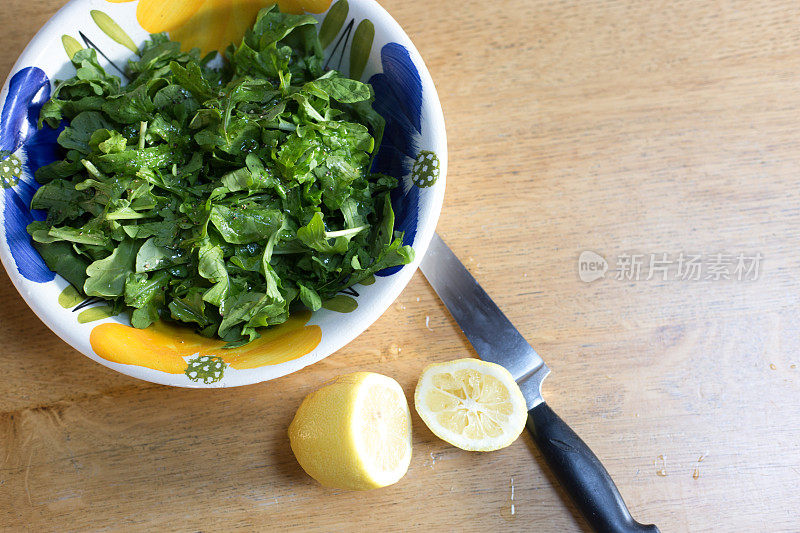 俯视图:芝麻菜沙拉在彩色碗，切柠檬，刀