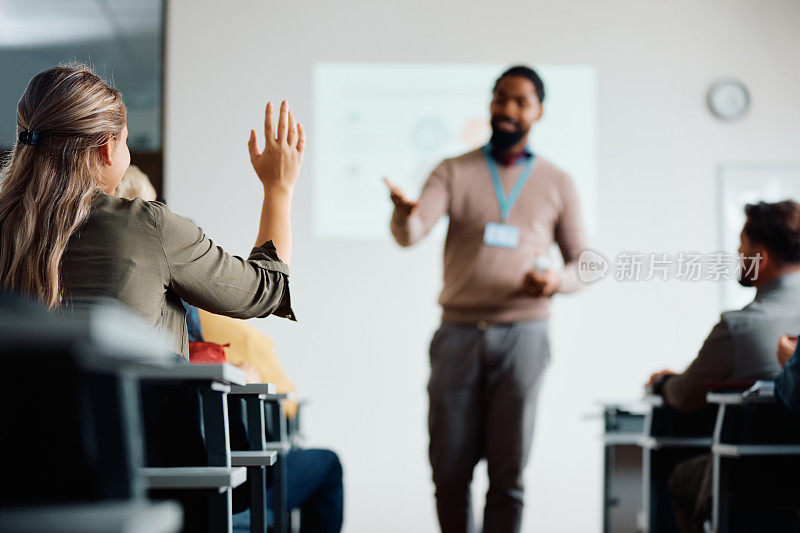 一名妇女在研讨会上举手提问的后视图。
