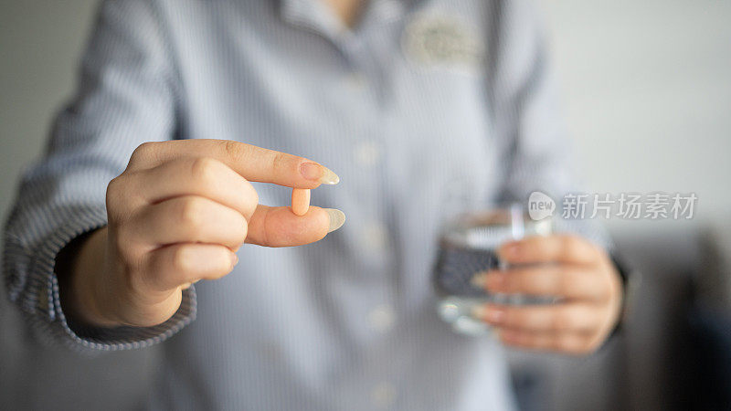 年轻女子拿着药片和一杯水在家里