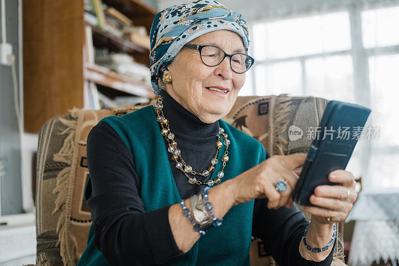 严肃成熟优雅的老年女性在家里沙发上拿着手机，看新闻或在线学习课程，用手机应用进行视频通话。