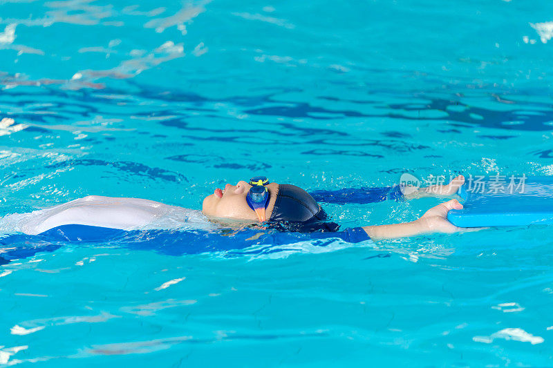 一个小男孩的活力去游泳池做仰泳练习。游泳池清澈的蓝色海水为他的水上活动提供了完美的背景。穿上泳装，戴上护目镜，自信地踏上健康之旅。