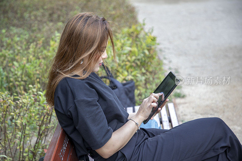 一个女人坐在公园的长椅上摆弄着她的平板电脑