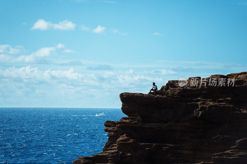 一个人坐在悬崖上欣赏海景