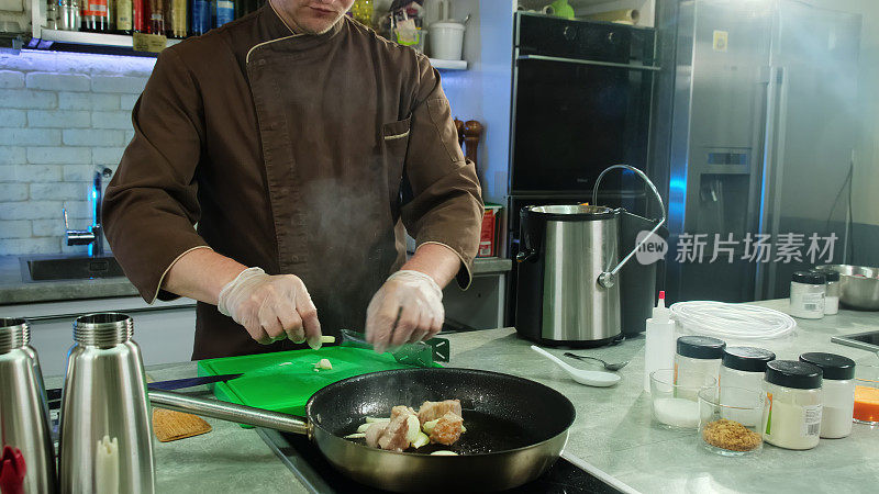 戴着手套的厨师把蒜瓣和肉一起放进锅里