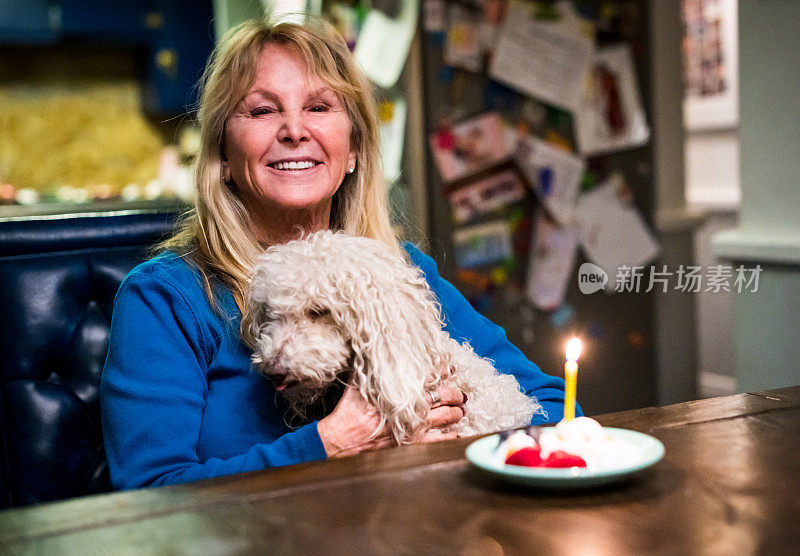 一个60多岁的成熟女人在家里吃着生日蛋糕，带着她的宠物狗过生日