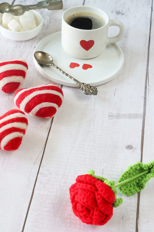 钩针玫瑰和心的特写形象，白色瓷杯和碟子与红心装饰，黑色浓缩咖啡，茶匙，糖碗，白糖块，糖钳，白色木纹背景，情人节和浪漫的概念