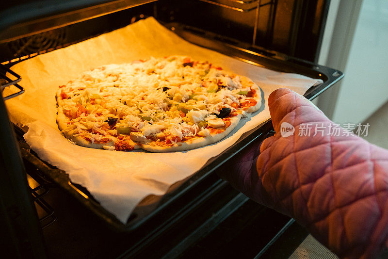 把自制披萨放入烤箱烹饪库存照片