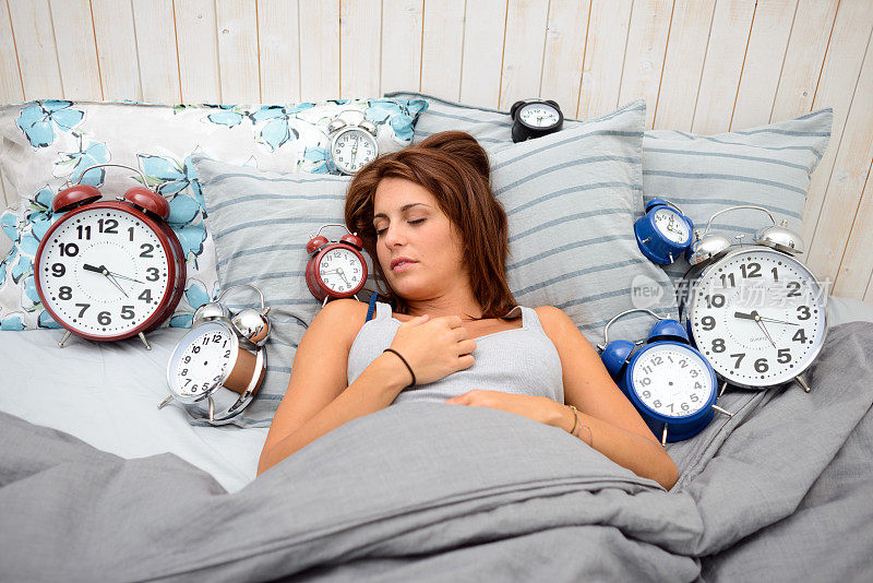 女人躺在床上，周围有很多闹钟