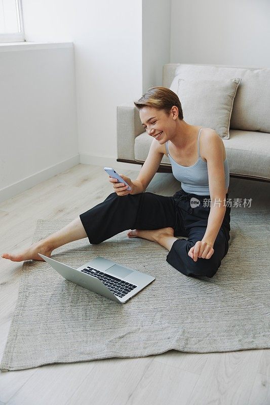 一个拥有笔记本电脑和手机的自由职业女性，穿着家常的衣服，剪着短发，坐在地板上工作，有自由的复印空间