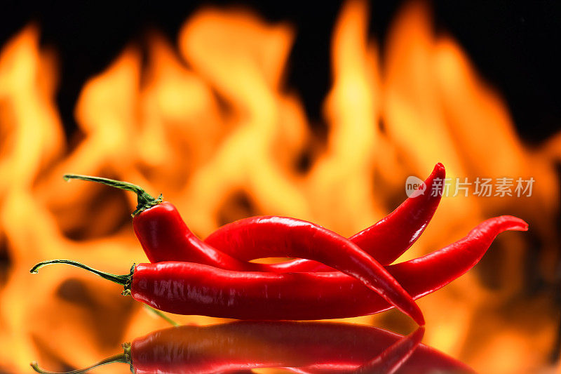 红辣椒，在燃烧的火的背景，火焰在黑色的背景，辛辣的香料