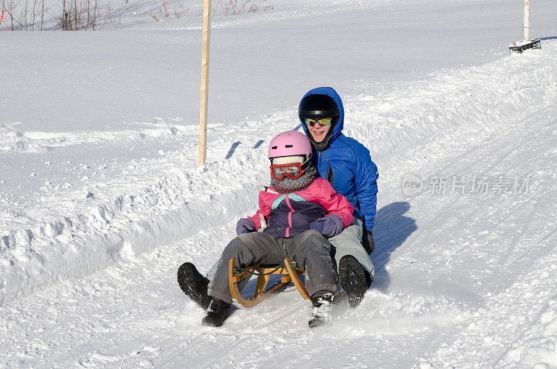 母亲和女儿滑下奥地利雪橇在冬天的白天