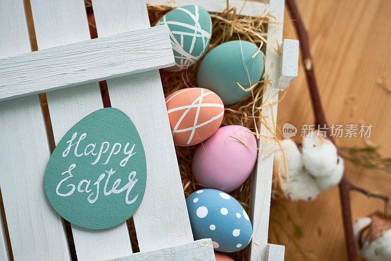 直接在上面观看彩色的彩蛋与点和条纹放置在与干草的木箱，在贺卡上的复活节快乐字母