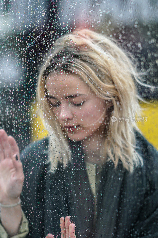一个年轻女子在雨天透过窗户看的肖像