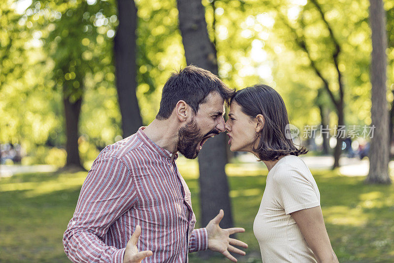 一对年轻夫妇在公园里吵架。年轻夫妇有一个夏天的一天争吵。站在公园外面，困惑的年轻女子打着手势，看着她的男朋友