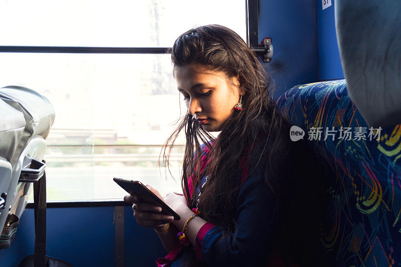 美丽的亚洲女孩旅行和使用智能手机在公交车上