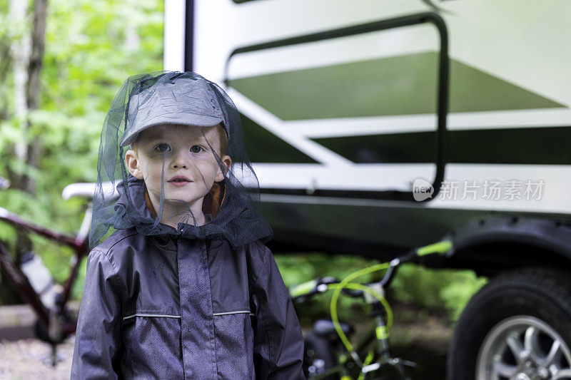 红发小男孩戴着蚊帐在露营地里玩耍