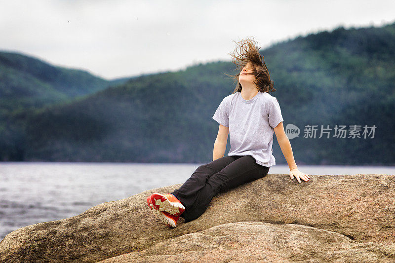 一个十几岁的小女孩独自坐在岩石上，经历着大风