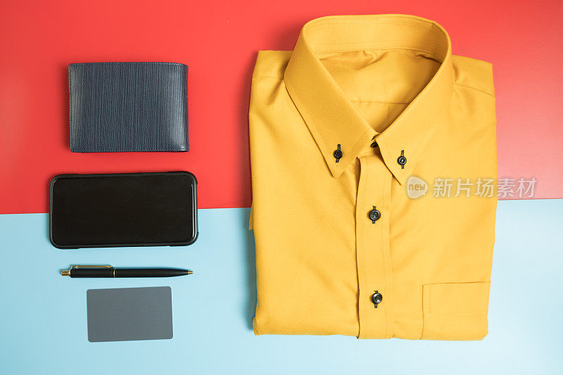 男士配饰:黄色衬衫，蓝色钱包，钢笔，手机和信用卡红蓝背景