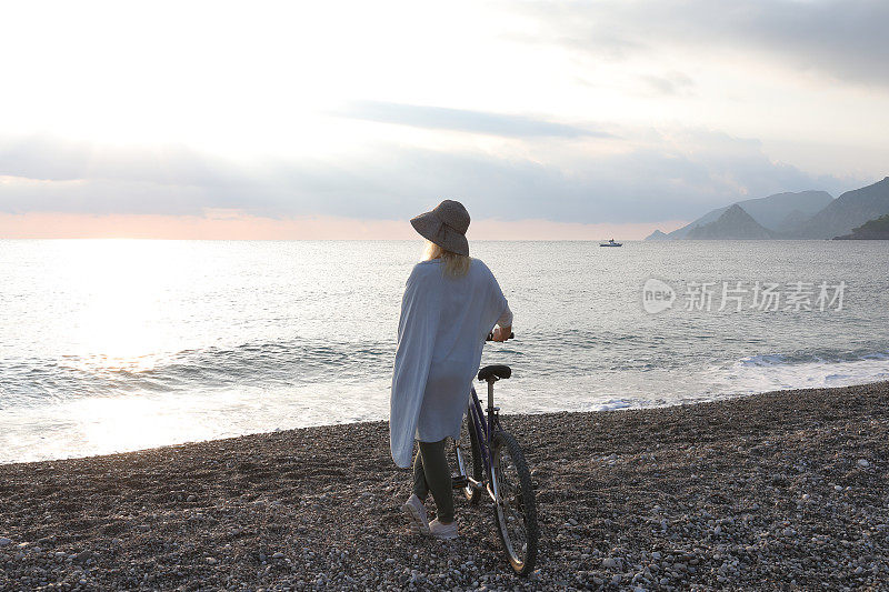 成熟的女人骑着自行车在日出的海滩上放松