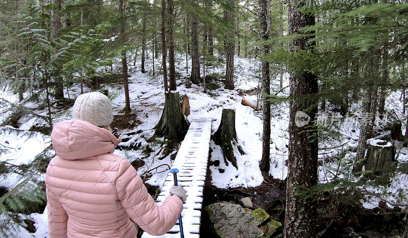 女性徒步旅行者走过被雪覆盖的木板路