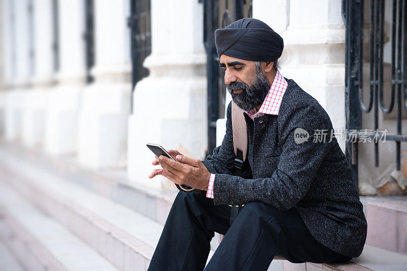 戴着头巾的丝绸商人用智能手机对抗建筑外部