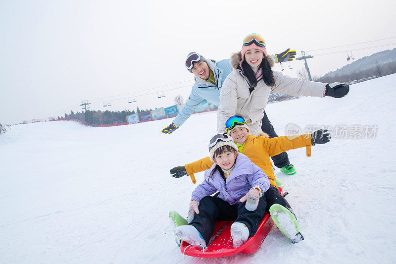 滑雪场上父母和坐在雪上滑板的孩子们
