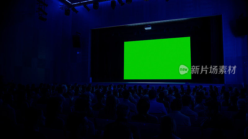 在现代电影院，观众在绿色屏幕上观看新大片。人们观看视频游戏比赛流媒体，现场音乐会视频，新产品发布预告片