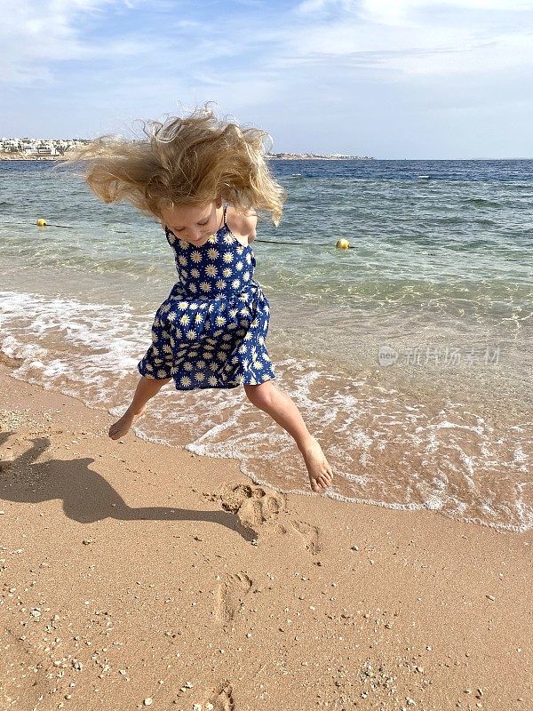小女孩在海边的沙滩上蹦蹦跳跳。