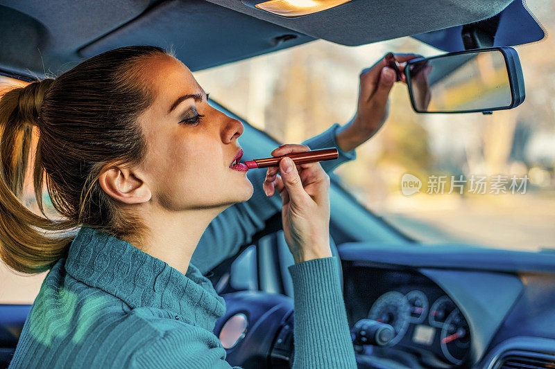 年轻优雅的女子在化妆时看着汽车视镜
