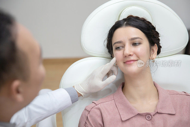 年轻漂亮的女人在美容院向美容师咨询抗衰老的治疗方法。医生指诊病人脸上的细纹和皱纹