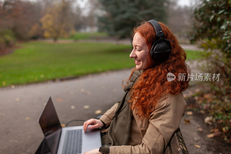 一个十几岁的学生戴着耳机坐在户外公园的长椅上进行放大会议