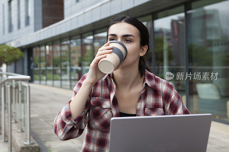 女大学生在校园里喝咖啡，用笔记本电脑