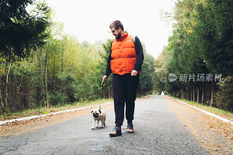 一个快乐的年轻人带着他的狗在森林里散步